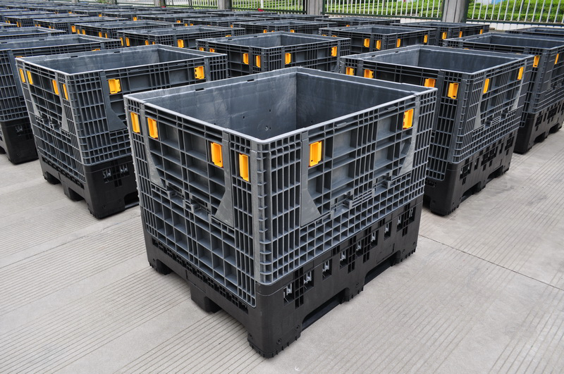 Foldable vs Fixed Plastic Pallet Boxes: An Engineering Comparison for Industrial Procurement 1 Rulyda collapsible bulk containers with yellow locking latches arranged in diagonal rows across an outdoor logistics yard, integrated black pallet bases with four-way forklift entry